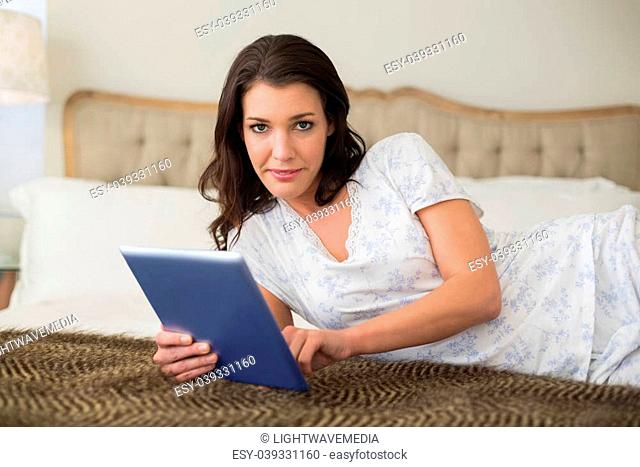 Serious pretty brown haired woman using a tablet pc in a chic bedroom