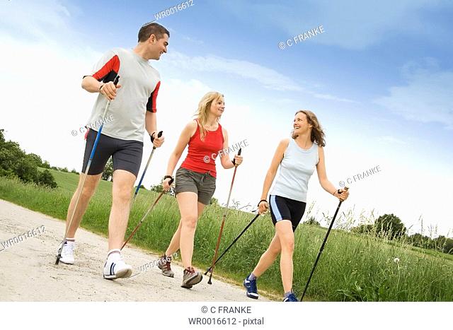 Two women and man walking with hiking poles on dirt road