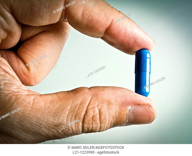 Blue pill between two fingers