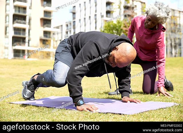 Senior woman assisting man doing exercise at public park