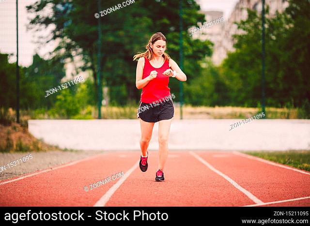 Beautiful young athlete Caucasian woman with big breast in red T-shirt and short shorts jogging, running in the stadium. Hairstyle of pony tail