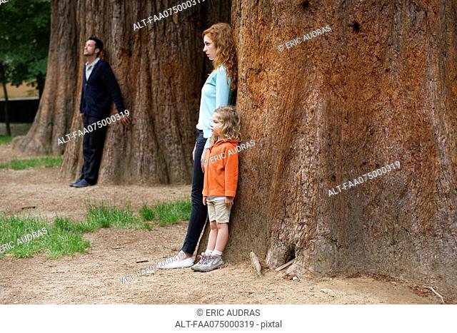 Mother and daughter leaning against tree, father standing separate in background