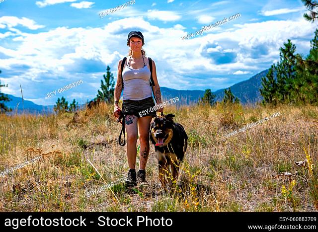 front view of a girl in the woods on a dirt road jogging with her beloved dog on a leash. with a panoramic view of the woods and the lake