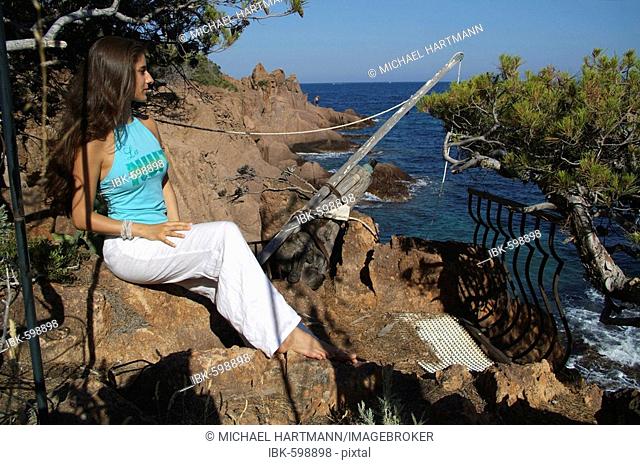 Young woman sitting against red cliff in a garden, Estérel Range on the Mediterranean, Théoule-sur-Mer, France, Europe