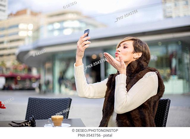 Woman doing a selfie outdoors in a Cafe, sending a kiss