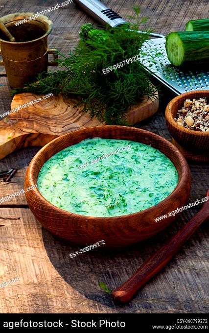 Homemade chilled tarator with ingredients on wooden rustic background. Traditional bulgarian summer cold soup with cucumbers, dill, garlic, yogurt and walnuts