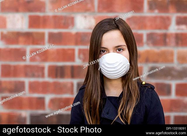 Young girl stands wearing a protective mask to protect against COVID-19 during the Coronavirus World Pandemic; Toronto, Ontario, Canada