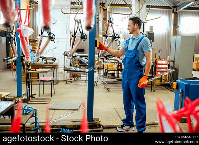 Bicycle factory, worker at bike assembly line. Male mechanic in uniform installs cycle parts in workshop, industrial manufacturing