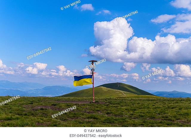 A pointer with a Ukrainian flag set at the peak of a big green mountain