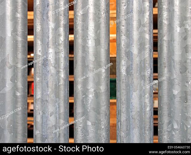 a close up of vertical galvanized steel fence with wooden pallets in outdoor storage visible between the gaps