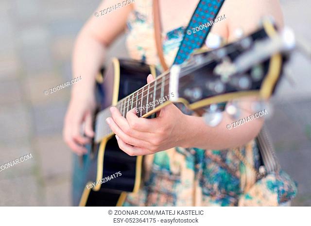 Female street musician playing guitar on sidewalk