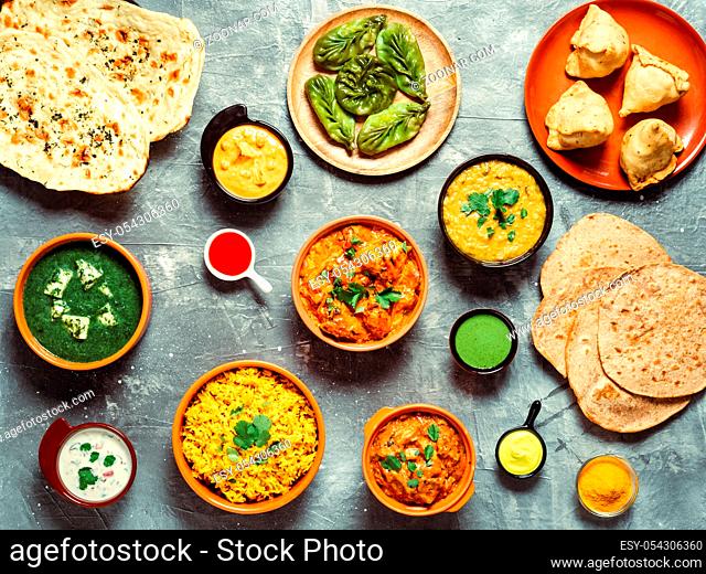 Indian cuisine dishes: tikka masala, dal, paneer, samosa, chapati, chutney, spices. Indian food on gray background. Assortment indian meal top view or flat lay