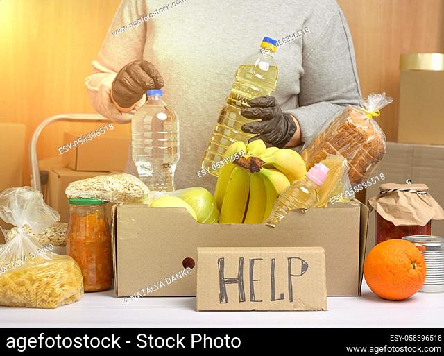 woman in a gray sweater is packing food in a cardboard box, the concept of assistance and volunteering, donation