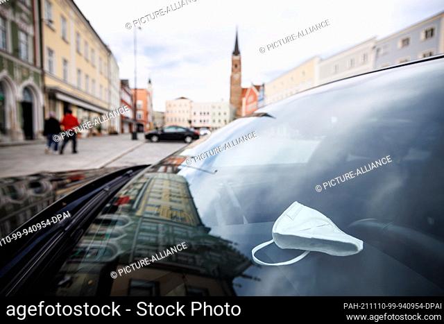 10 November 2021, Bavaria, Eggenfelden: An FFP2 mask lies on a dashboard of a vehicle on the town square, while the Catholic parish church of St