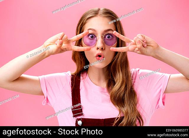 Woman liking how sunglasses finished outfit. Portrait of charming playful and charismatic young girl in blue eyewear with wavy pretty hair showing peace...
