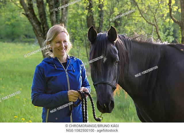 blonde woman with black Arabian horse in a ray of sunlight