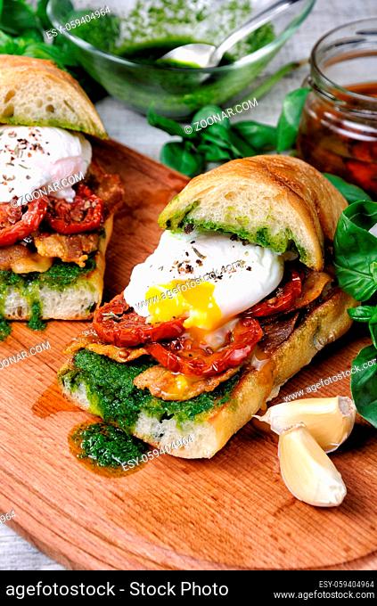 Toasted ciabatta with pesto, slices of bacon, sun-dried tomatoes and poached egg