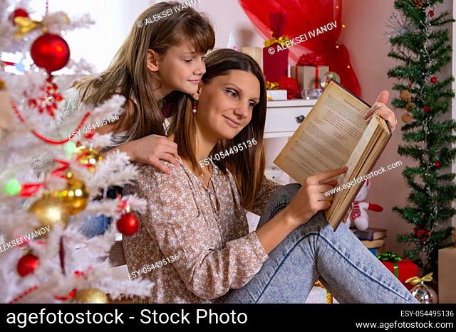 Mom and daughter read a book near a Christmas tree