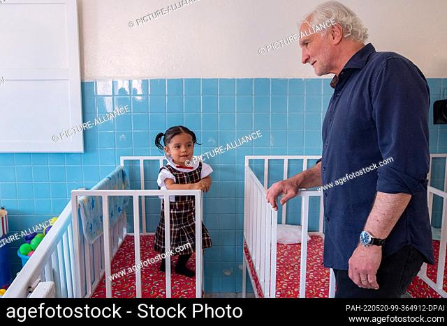 19 May 2022, Mexico, Queretaro: Soccer icon Rudi Völler (r) stands next to a little girl in her crib during his visit to the Casa de Cuna orphanage