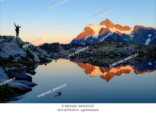 Jubilant hiker and reflection of Mount Shuksan in alpine tarn, Mount Baker-Snoqualmie National Forest, Washington, United States of America