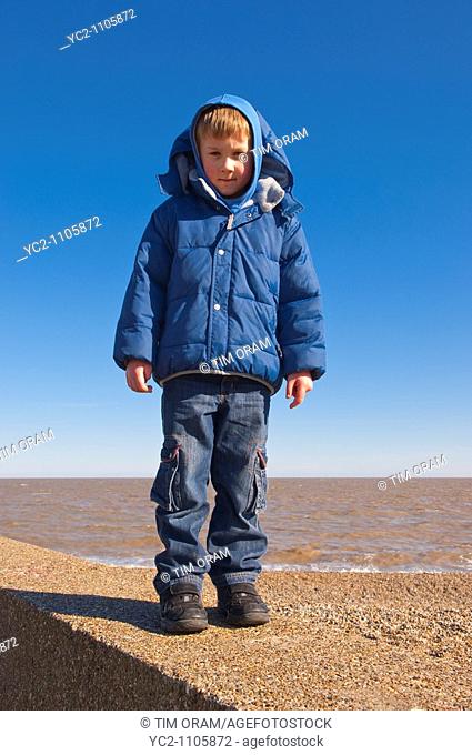 A  picture of a 6 year old boy standing on the sea wall on a uk beach