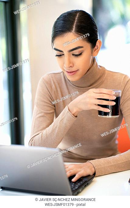 Young woman having a drink and using laptop in a cafe