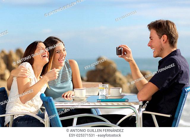 Friends on vacations laughing and taking photo with a smart phone in a restaurant on the beach