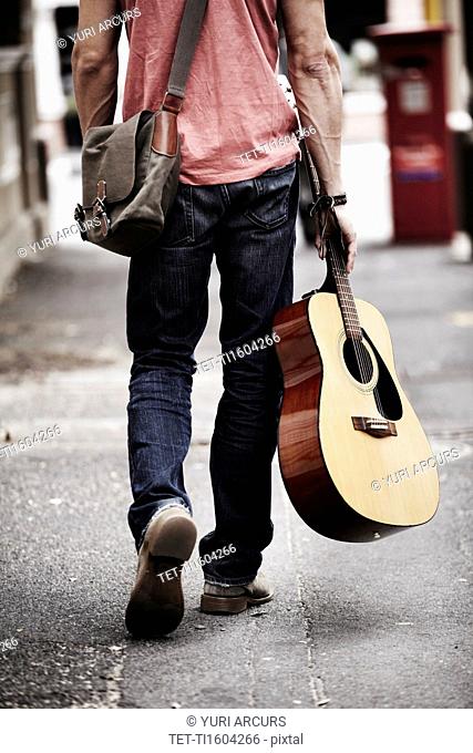 Man with guitar walking down street