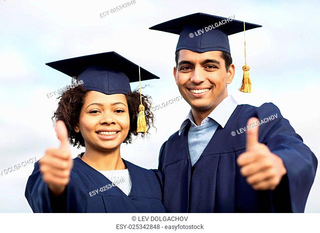 education, graduation, gesture and people concept - happy international students in mortar boards and bachelor gowns outdoors showing thumbs up