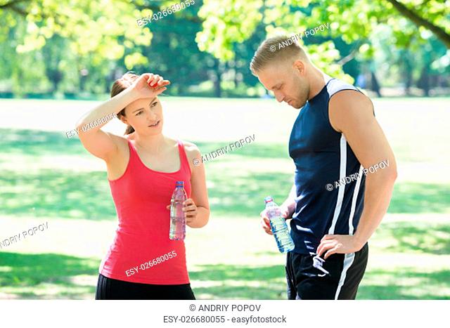 Young Tired Couple Standing In Park Holding Bottles Of Water