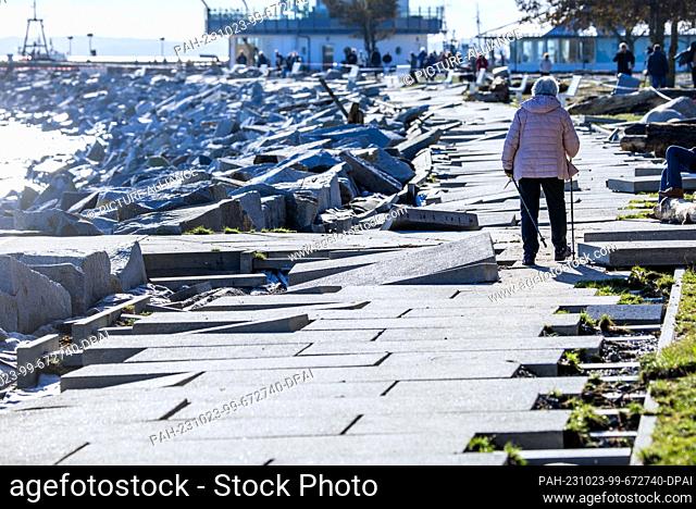 23 October 2023, Mecklenburg-Western Pomerania, Sassnitz: A woman walks across the sidewalk slabs on the closed-off boardwalk at the harbor that were washed...