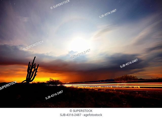 During a nighttime thunderstorm, a halo forms around the moon as cars drive down the Tucson - Ajo Highway, east of Tucson, Arizona