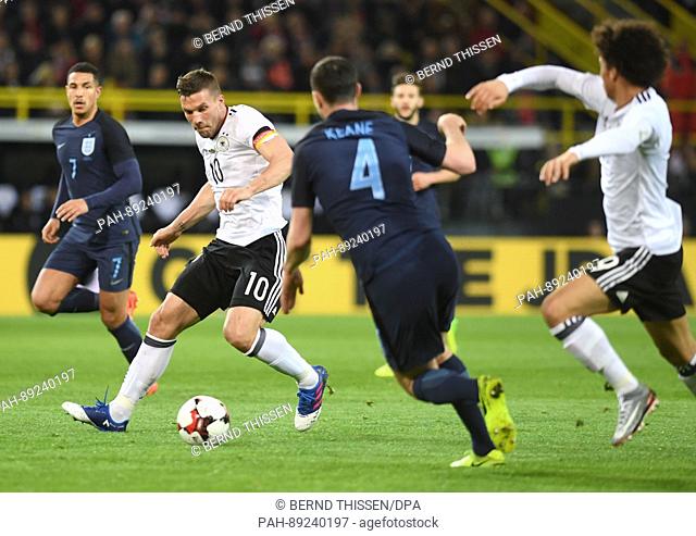 Germany's Lukas Podolski plays against England's Jake Livermore (L) and Michael Keane during the international match between Germany and England at Signal Iduna...