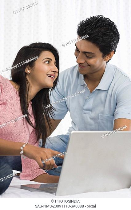Couple smiling in front of a laptop on the bed