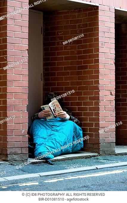 A homeless man reading a book while in his sleeping bag