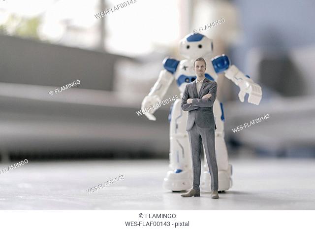 Miniature businessman figurine standing in front of robot