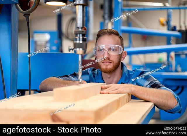 Portrait of carpenter wearing protective goggles drilling wooden plank
