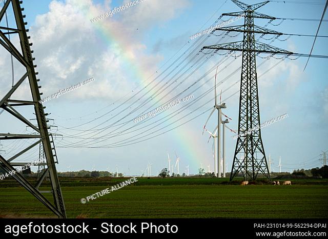 14 October 2023, Schleswig-Holstein, Wöhrden: A rainbow between high-voltage pylons and wind turbines. The west coast line from the Danish border to Brunsbüttel