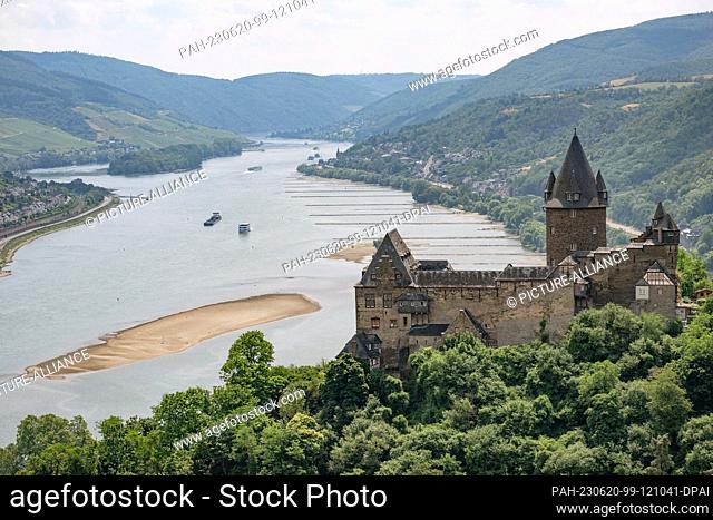 20 June 2023, Rhineland-Palatinate, Bacharach: Ships sail past Stahleck Castle on the Rhine. A large sandbank can be seen in the river