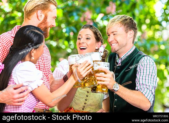Friends, two men, two women, standing in beer garden clinking glasses with beer