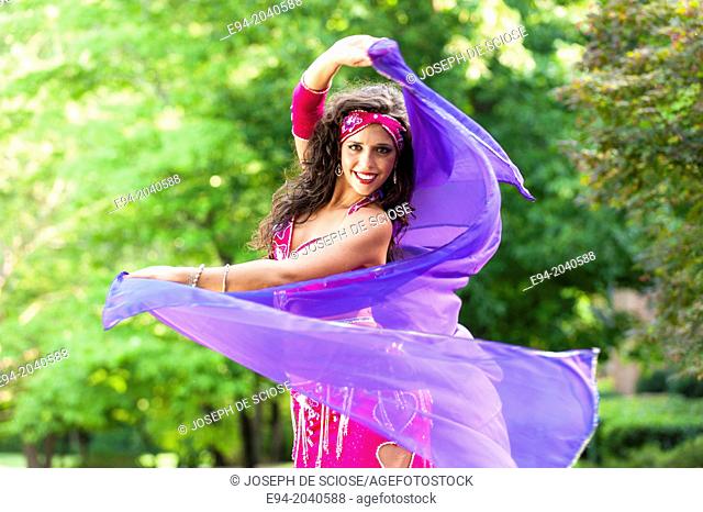 A 23 year old brunette woman in costume belly dancing outdoors