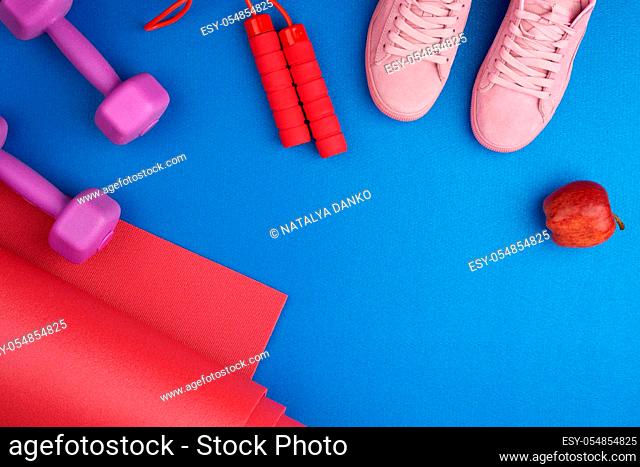 pair of pink training sneakers with laces, purple plastic dumbbells, red twisted neoprene mat on a blue texture background, top view, sports set