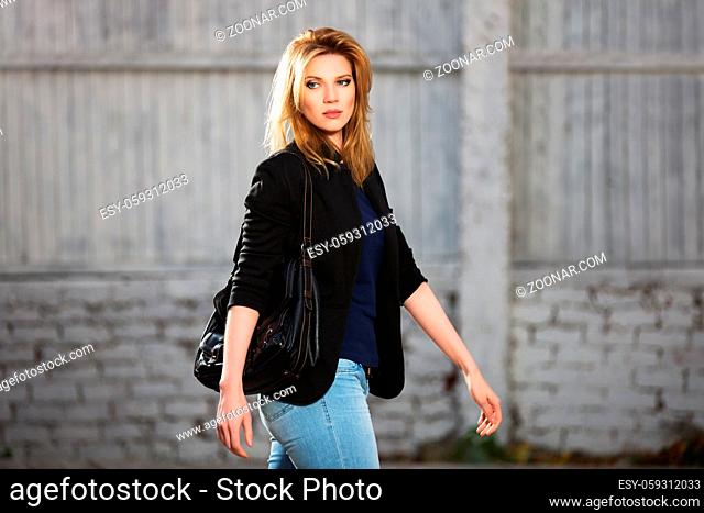 Young fashion blond business woman with handbag walking on city street