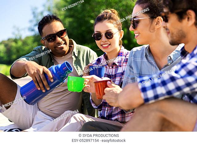 happy friends drinking tea from thermos in summer