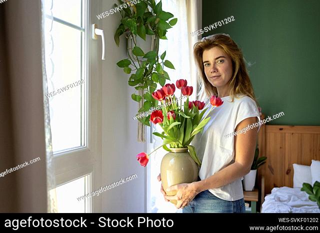 Smiling woman standing with bouquet of tulips at home