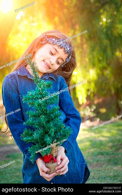Cute Mixed Race Young Girl Holding Small Christmas Tree Outdoors
