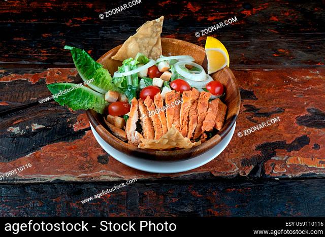 Greek salad with grilled chicken isolated on rustic wooden kitchen table