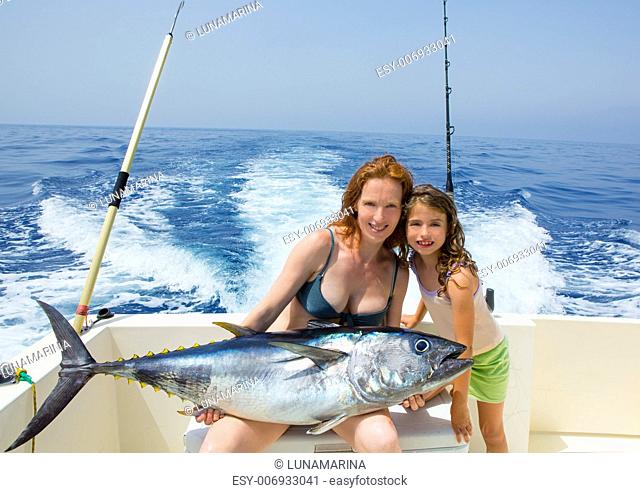 bikini fisher woman and daughter girl holding big bluefin tuna catch on boat deck