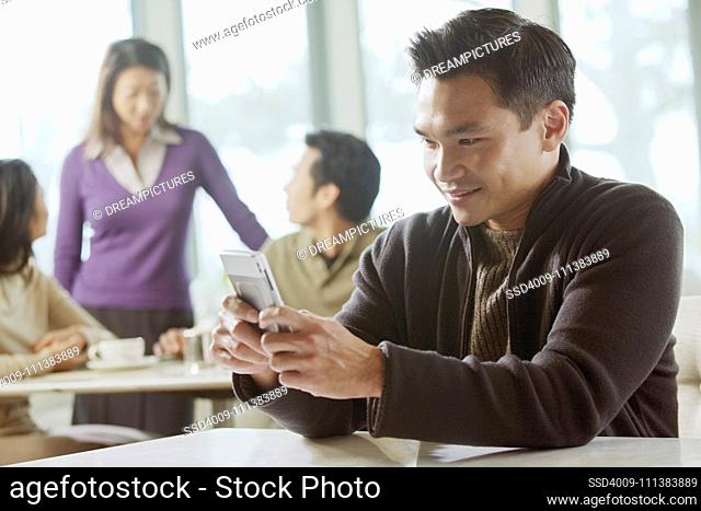 Asian man text messaging on cell phone in cafe