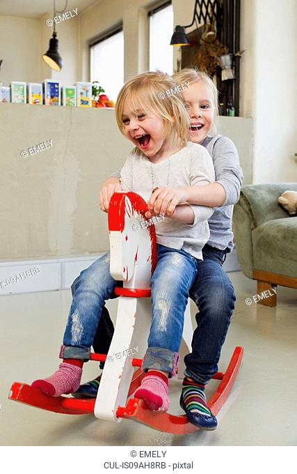 Two young sisters playing on rocking horse